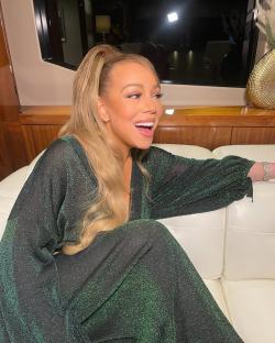 Mariah Carey laughing while sitting on a couch.